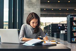 Person writing on notebook at table in library,